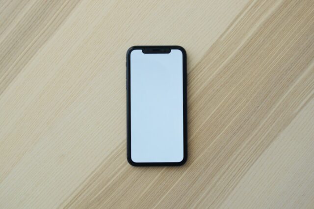 Een telefoon met een leeg scherm ligt op een licht houten tafelblad