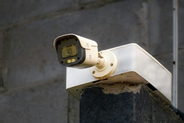 Een witte beveiligingscamera hangt aan een betonnen muur en kijkt naar beneden